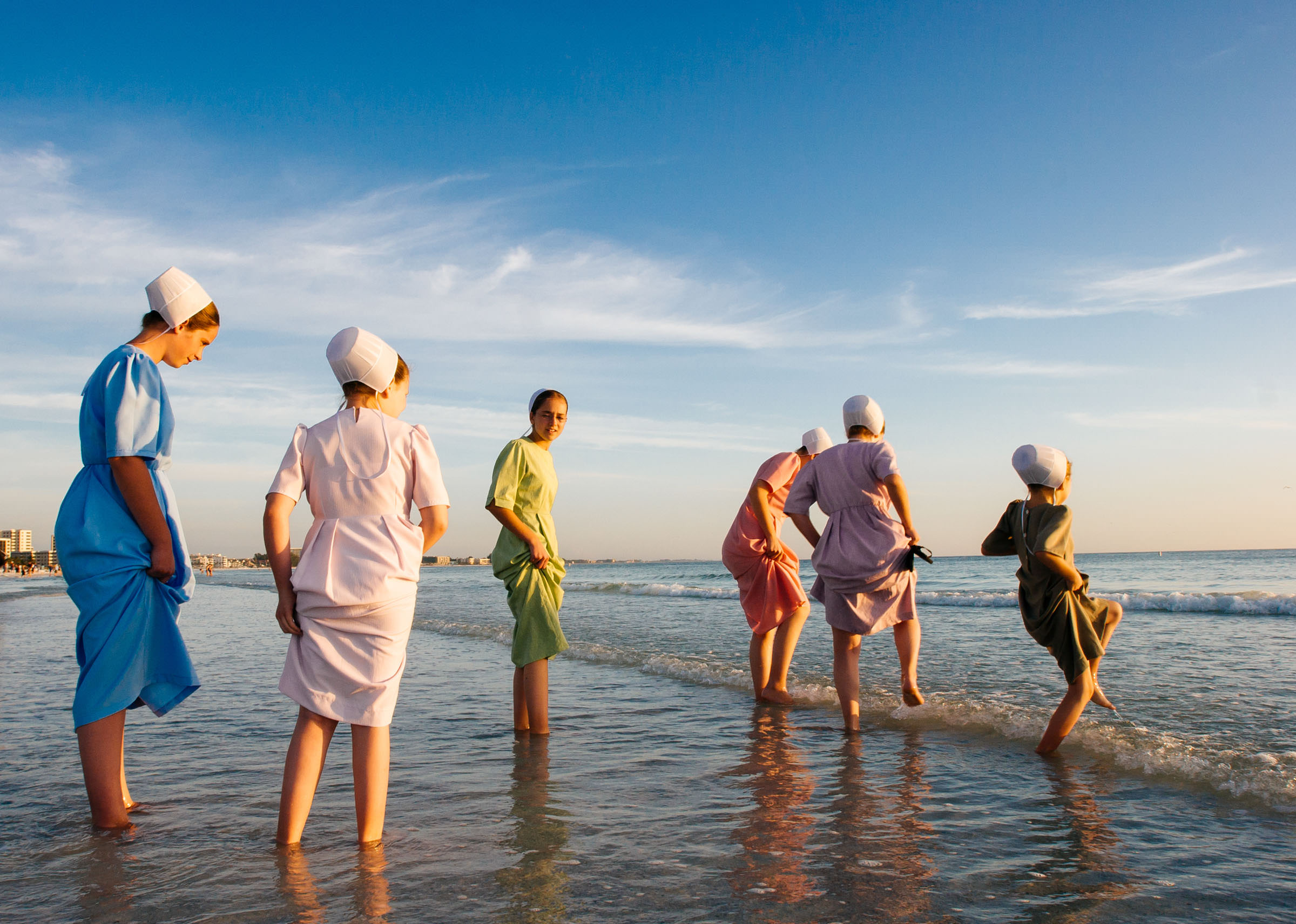 A group of young Amish women dip their toes in the ocean while walking along Siesta Key Beach on a warm January afternoon in Florida, where Amish and Mennonite families travel every winter to escape the cold.